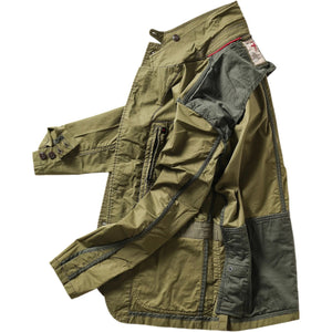 A person models the RELWEN Flyweight Flex Blazer in Burnt Olive over a blue and white checkered shirt with gray pants, hands in pockets, against a plain white background.