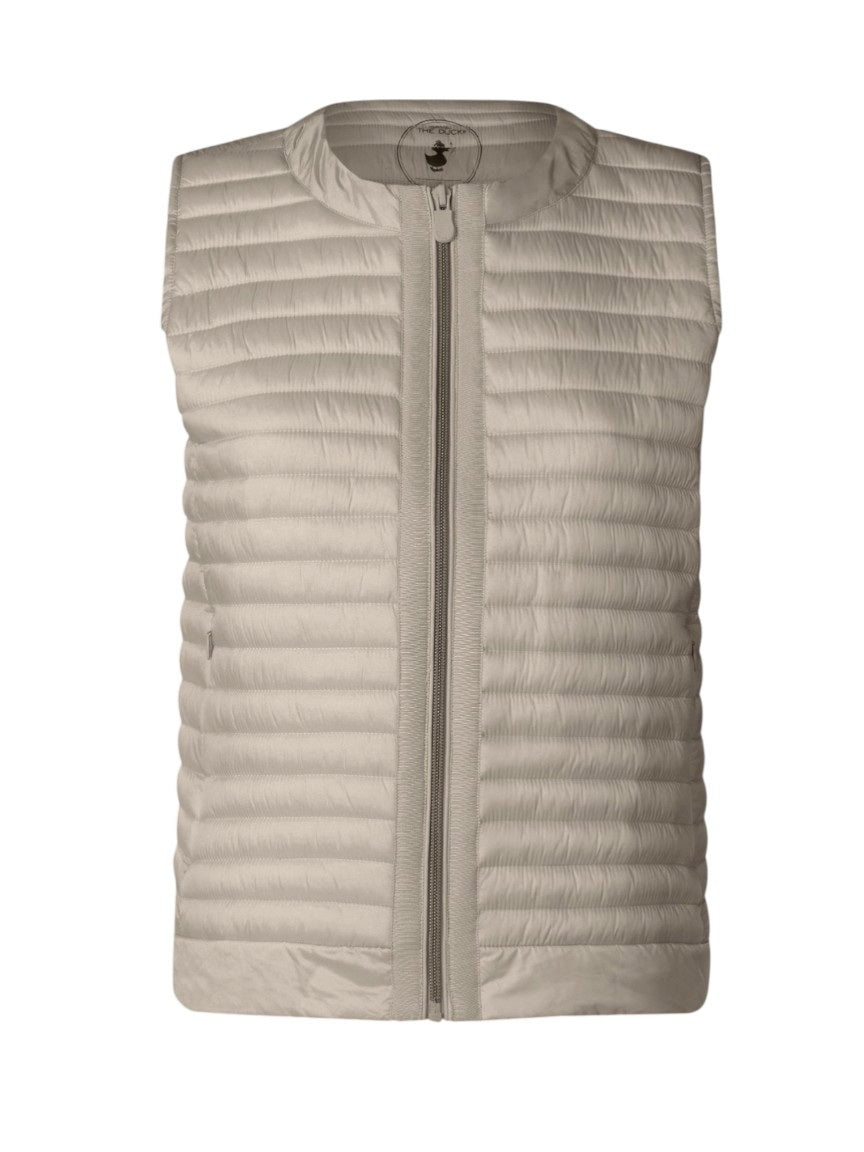 A woman with short brown hair wears the SAVE THE DUCK MARA PUFFER VEST over a white t-shirt and beige pants, standing against a plain light background and looking at the camera with a neutral expression.