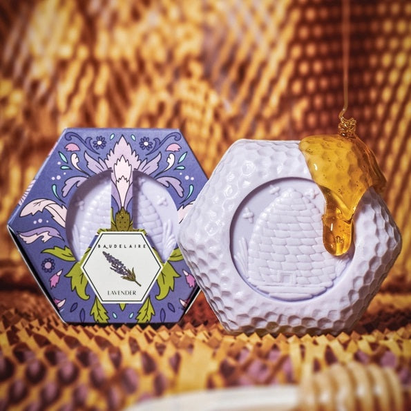 Experience the luxurious BAUDELAIRE - LAVENDER HONEY SOAP 3.5 OZ, HEX BOX—a triple-milled bar delicately scented with lavender. Presented in a hexagonal purple box adorned with elegant floral designs and a central lavender flower illustration, this nourishing soap from BAUDELAIRE offers a gentle and soothing cleanse.