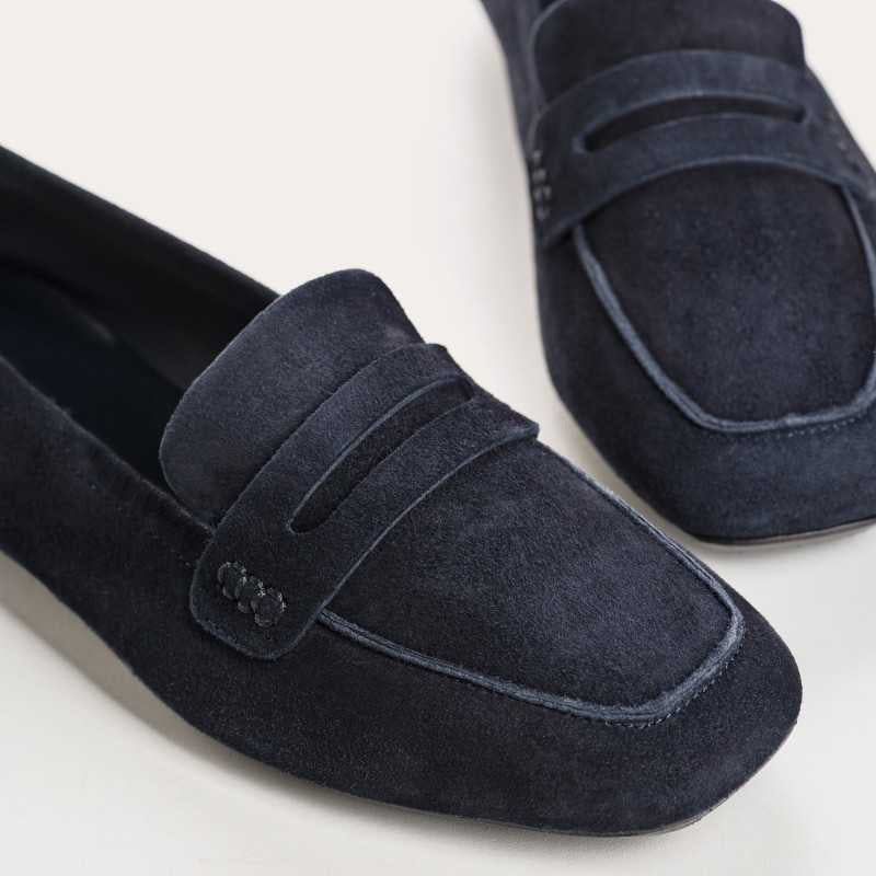 Six pairs of REQINS HEMA suede loafers in marine, featuring a classic penny loafer design and timeless silhouette, are displayed on a light tan surface in various blue and green shades.
