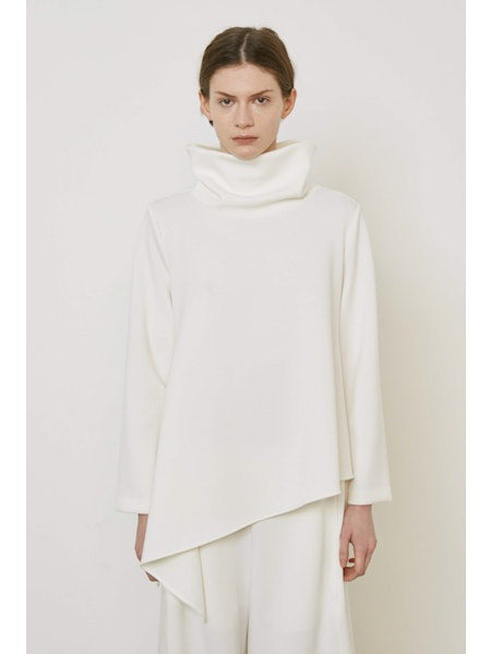 A person with brown hair faces away wearing the MEIMEIJ ASYMMETRICAL COWLNECK TOP in lightweight scuba fabric, featuring an asymmetrical hem, paired with matching white bottoms, against a plain white background.