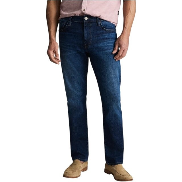 A man with gray hair, wearing a light pink polo shirt, 34 HERITAGE - CAMINO Relaxed Straight Jeans in Dark Vintage featuring classic contrast stitching, and tan loafers stands facing away against a light background.