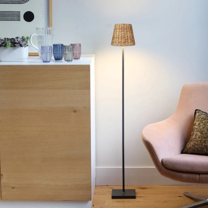 A modern poolside area features white lounge chairs, a potted fern, EMPIRE Water Hyacinth Woven Wicker Shade XXL by Zafferano America, white swan float, and a cordless lamp with glass water bottle on the table.