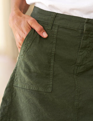 The FRANK & EILEEN Jameson Utility Skirt in Hunter Green, knee-length and made of Italian Performance Linen, features utility pockets, belt loops, and visible stitching. Shown laid flat on a white background.