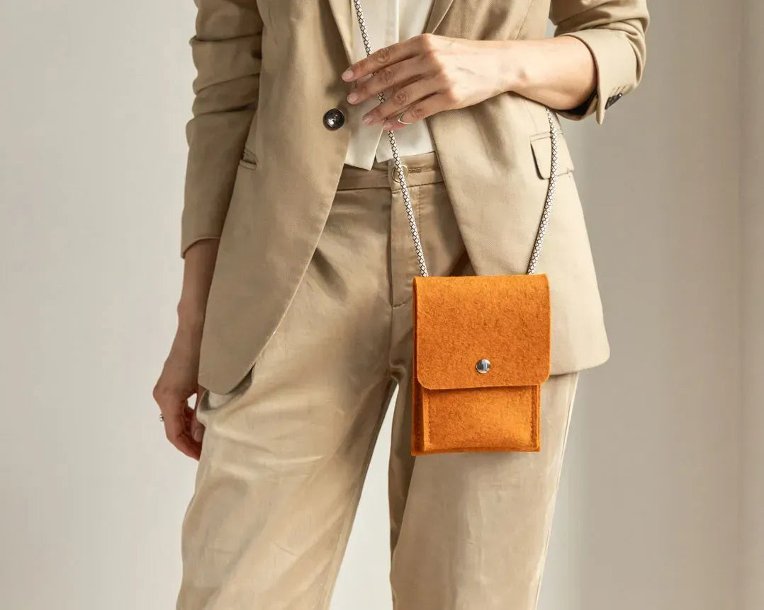 A person in a loose gray shirt and taupe pants carries the WOOLBERRY WOOL FELT PHONE BAG—a pink crossbody with a flap and silver chain—over their shoulder, showing only their torso and part of their arms.