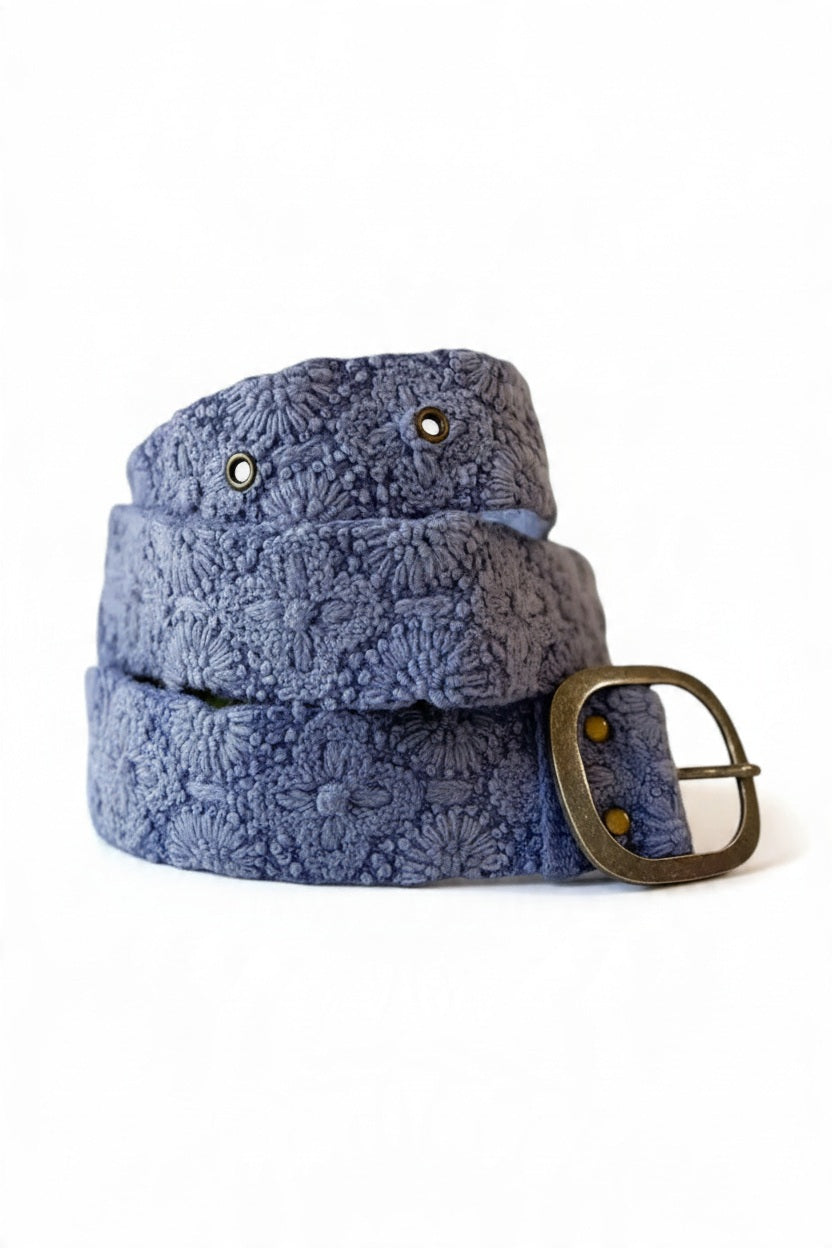 The JENNY KRAUSS - AZURE SEAS EMBROIDERED WOOL BELT by JENNY KRAUSS features an embroidered floral pattern, an adjustable waist, and a silver rectangular buckle, shown coiled on a white surface.