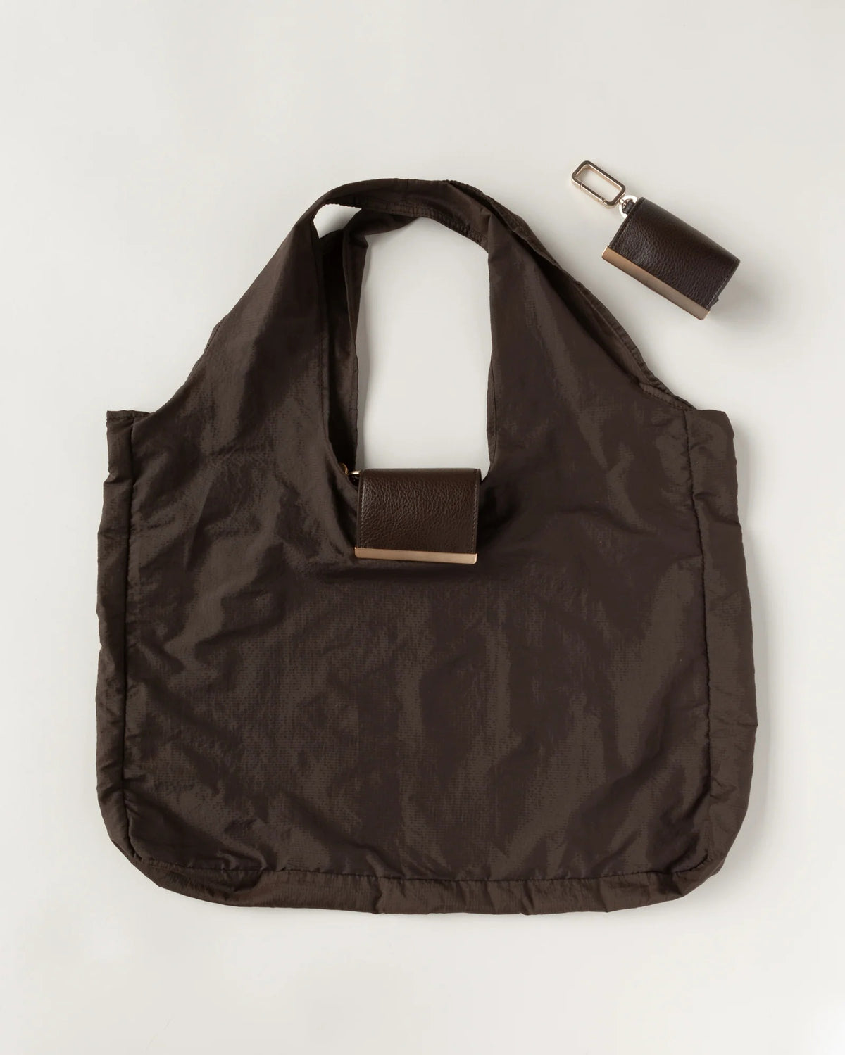 The KEOTE - KEYCHAIN TOTE IN ESPRESSO by KEOTE is a dark brown compact tote with two handles, featuring a detachable rectangular case in the center and an additional closed keychain tote, displayed on a light background.