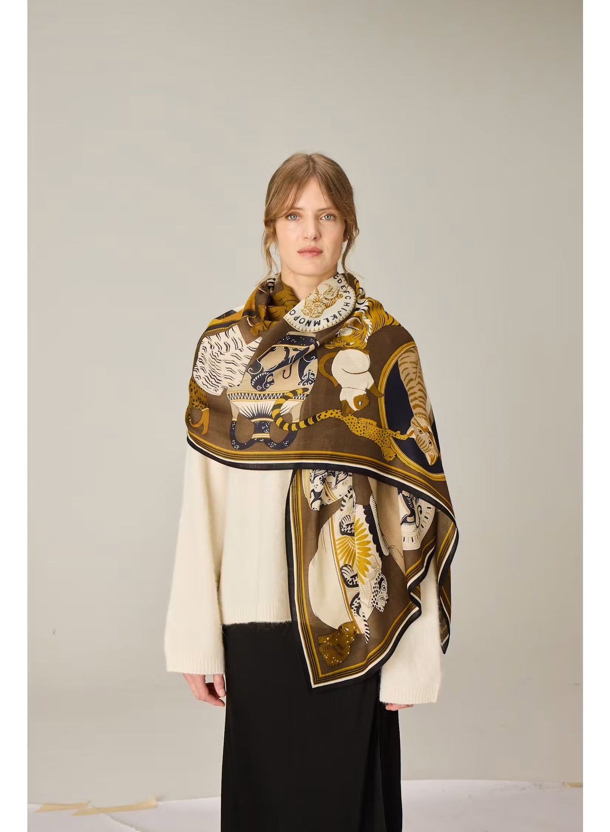 The INOUI EDITIONS - COLLECTIONNEUR Wool Scarf with Cats in Khaki by INOUI is a rectangular accessory crafted in India from 100% wool. It features an artistic collage-like pattern of illustrated cats and circular motifs in shades of gold, white, black, and gray set against a dark khaki background. Measuring 70 x 190 cm, this striking scarf adds both warmth and a touch of artistry to any ensemble.