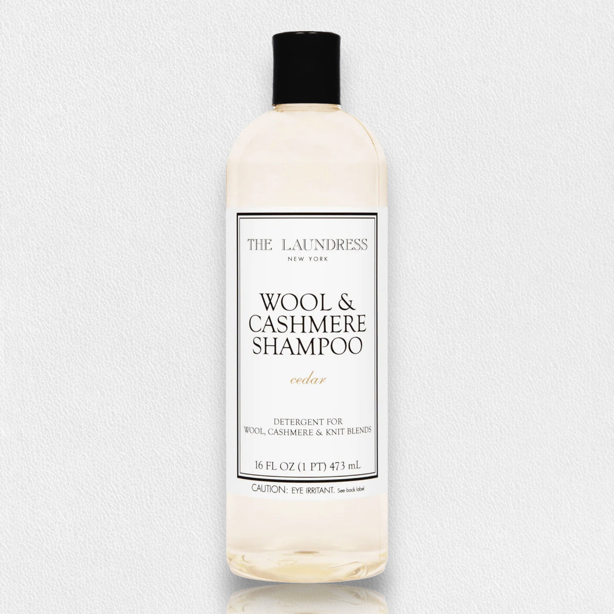 A 16 fl oz (473 ml) bottle of THE LAUNDRESS - WOOL AND CASHMERE SHAMPOO 16OZ, featuring a cedar scent. The clear bottle is topped with a black cap and has a white label with black text specifying the brand, THE LAUNDRESS, and product type. This gentle wash detergent, formulated with bio-based ingredients, is ideal for wool, cashmere, and knit blends.