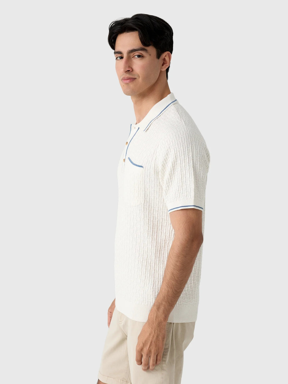 A smiling gray-haired man in sunglasses and khaki pants wears the CRIQUET Bungalow Sweater Polo in White, featuring a blue-trimmed collar and pocket, standing against a plain background.