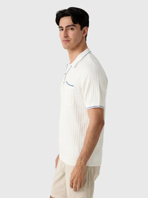 A smiling gray-haired man in sunglasses and khaki pants wears the CRIQUET Bungalow Sweater Polo in White, featuring a blue-trimmed collar and pocket, standing against a plain background.