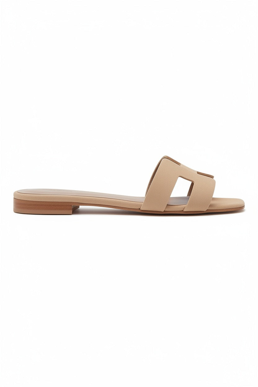 The MICHELE LOPRIORE - H SLIDE is a brown leather sandal with two wide straps, including one with a rectangular cutout, featuring a flat wooden sole. Made in Italy by MICHELE LOPRIORE, it's shown on a white background.