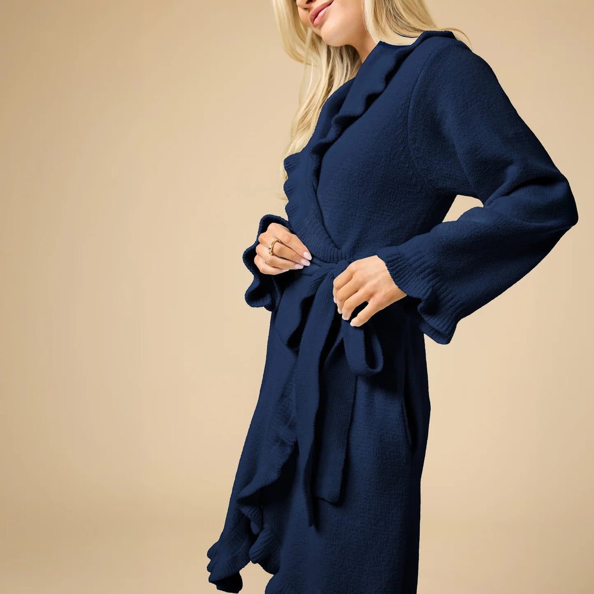 A woman wearing a SOFTIES - RUFFLE CHENILLE ROBE 36″ IN MIDNIGHT, a knee-length navy blue chenille robe with cascading ruffle trim.