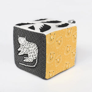 The WEE GALLERY - JUNGLE SOFT BLOCK by WEE GALLERY is a soft fabric cube perfect for stimulating a baby's developing senses. It features monochrome patterns and playful designs, including a cute monkey illustration on one side and a yellow leaf on another. Inspired by jungle life and animals, this toy boasts various textures and small loops on top for easy grasping.
