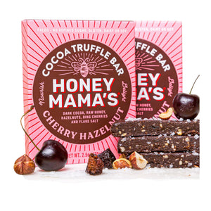 A square package of HONEY MAMA’S - CHERRY HAZELNUT TRUFFLE BAR features a bee graphic with a pink and red design, highlighting it as a limited edition, gluten-free, and dairy-free chocolate bar made with Bing cherries and toasted hazelnuts.