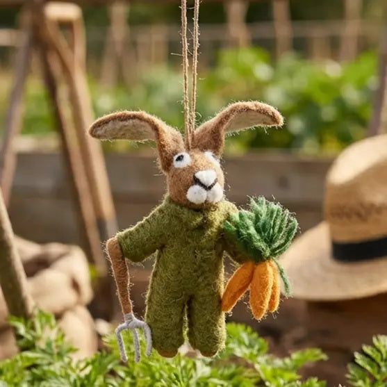 GORDON THE GARDENING HARE ORNAMENT by FELT SO GOOD, a felt hare wearing green overalls, holding a small garden fork and a bundle of carrots.