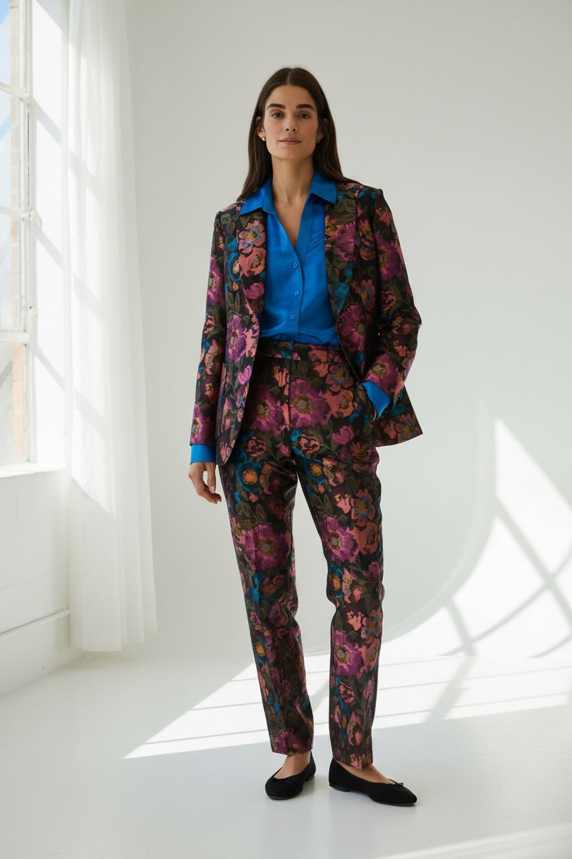 A woman with long brown hair is wearing the HINSON WU - CORINNE JACQUARD JACKET IN FLORAL BOUQUET, paired with a bright blue satin shirt underneath, standing against a plain light background.