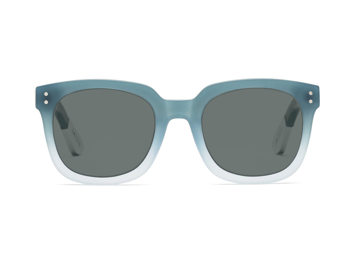 The CADDIS Jockamo Polarized Sunglasses feature a blue-green rectangular design with dark polarized lenses. The premium acetate frame is accented by white-tipped arms, and the brand "Caddis" is prominently displayed on both the lens and arm. These sunglasses combine a vintage aesthetic with a modern, sleek design perfect for casual wear.