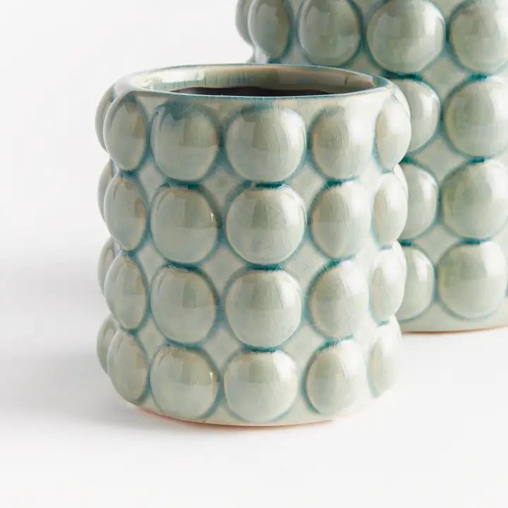 The NAPA HOME AND GARDEN - VALENCIA POT, SMALL by NAPA HOME AND GARDEN is a light green contemporary planter with a glossy seafoam glaze and a textured surface featuring raised circular bumps arranged in a grid pattern.
