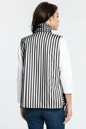 A woman with short dark hair stands sideways and looks at the camera against a plain white background, wearing the HINSON WU LAUREN REVERSIBLE VEST— a blue and white checkered quilted cotton vest by HINSON WU— layered over a white long-sleeve shirt and jeans.