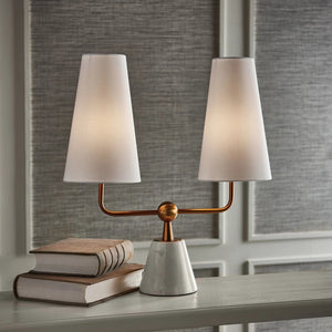 Introducing the Madison Dublet Lamp by NAPA HOME AND GARDEN, showcasing a modern design with two white conical shades on a gold bar. Its marble base and brass finish provide sophistication against a plain white background.
