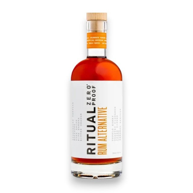 A bottle of RITUAL ZERO PROOF - RUM ALTERNATIVE, a non-alcoholic rum from RITUAL ZERO PROOF, featuring an orange liquid, a wooden cap, and a white label with the brand name displayed vertically alongside small-print flavor notes.