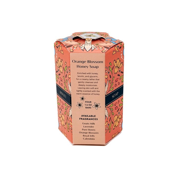 Hexagonal pink soaps with a honeycomb pattern are stacked beside a decorative orange and pink box labeled “BAUDELAIRE - ORANGE BLOSSOM HONEY SOAP 1.4 OZ QUARTET.” Each bar in this luxurious BAUDELAIRE set is triple-milled for rich lather and long-lasting Orange Blossom fragrance. The intricate floral designs on the box are complemented by a distinctive floral badge on top.