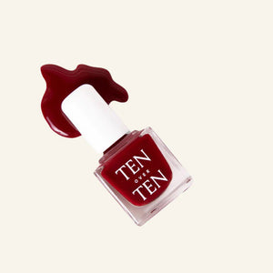 A glass bottle of TENOVERTEN - NAIL POLISH from the brand TEN OVER TEN, featuring a white cap and a dusty pink nail color. The front label displays "TEN OVER TEN" in white uppercase letters. This vegan, eight-free formula ensures both beauty and peace of mind. The background is plain and light-colored.