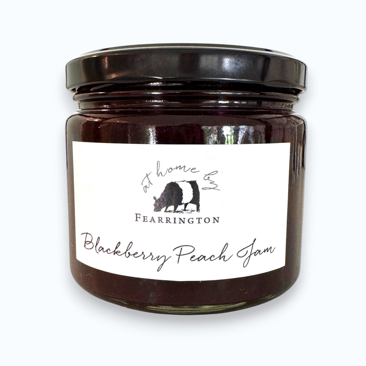 A glass jar of FEARRINGTON SIGNATURE COLLECTION - FEARRINGTON HOUSEMADE BLACKBERRY PEACH JAM with a black lid and a white label. The label lists ingredients: blackberries, peaches, lemon, cinnamon, nutmeg, sugar, pectin. It also mentions: "Handmade with care in our kitchens by Fearrington chefs." Perfect as a hostess gift or for breakfast jams. May contain allergens.