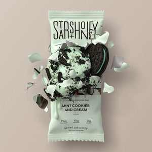 A STARS+HONEY - MINT COOKIES & CREAM Collagen Protein Bar, with its wrapper, displays mint chocolate ice cream and cookie pieces bursting out for a dynamic effect against a beige background.