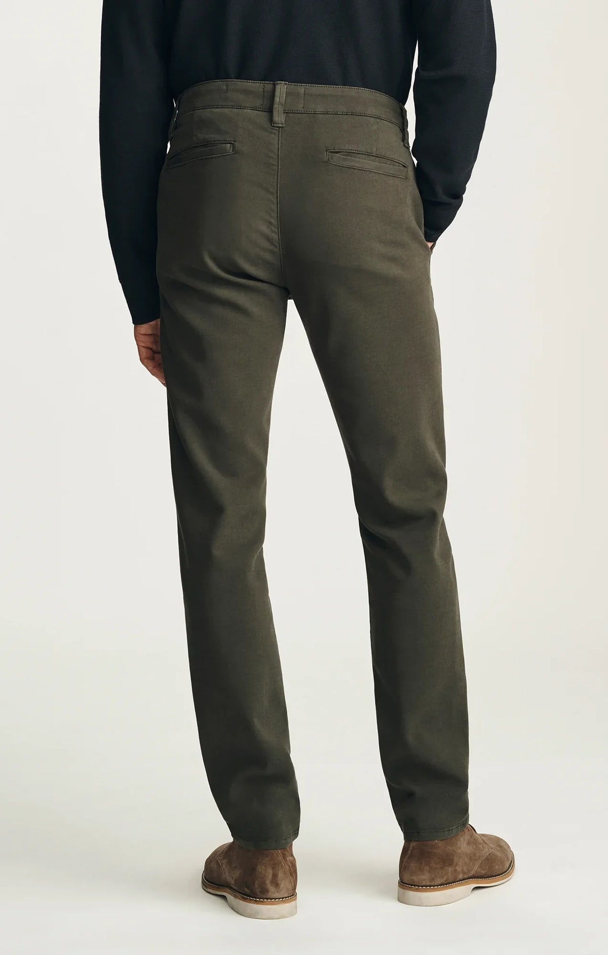 A person stands with their back to the camera against a neutral background, wearing the 34 HERITAGE - VERONA Straight Leg Chino Pant in Jasper High Flyer paired with a black long-sleeve shirt and brown suede shoes.
