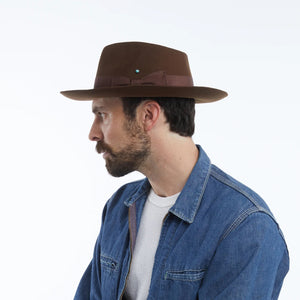 The WYETH - TEDDY HAT IN BROWN by WYETH is a vintage-inspired wide-brimmed fedora with a matching dark brown ribbon band, shown against a plain white background.