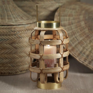 The ZODAX Bamboo Lantern with Brass Trim is a decorative lantern featuring a rustic design. It has a woven, cage-like structure made of bamboo slats held together with red twine. The lantern boasts a brass base, top, and handle, creating a harmonious blend of natural and metallic aesthetics. Dimensions: 20.32 cm x 20.32 cm x 33.02 cm (8 in x 8 in x 13 in).