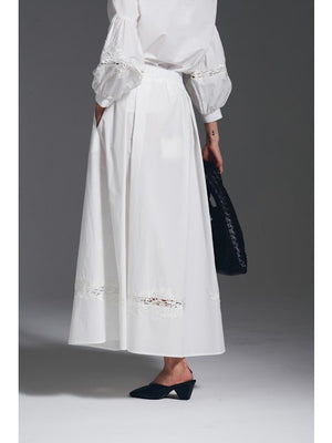 The MILVA MI Cotton Midi Skirt in Black by MILVA features a solid, subtly textured surface with slight shade variations and an elegant embroidered cutwork hem.
