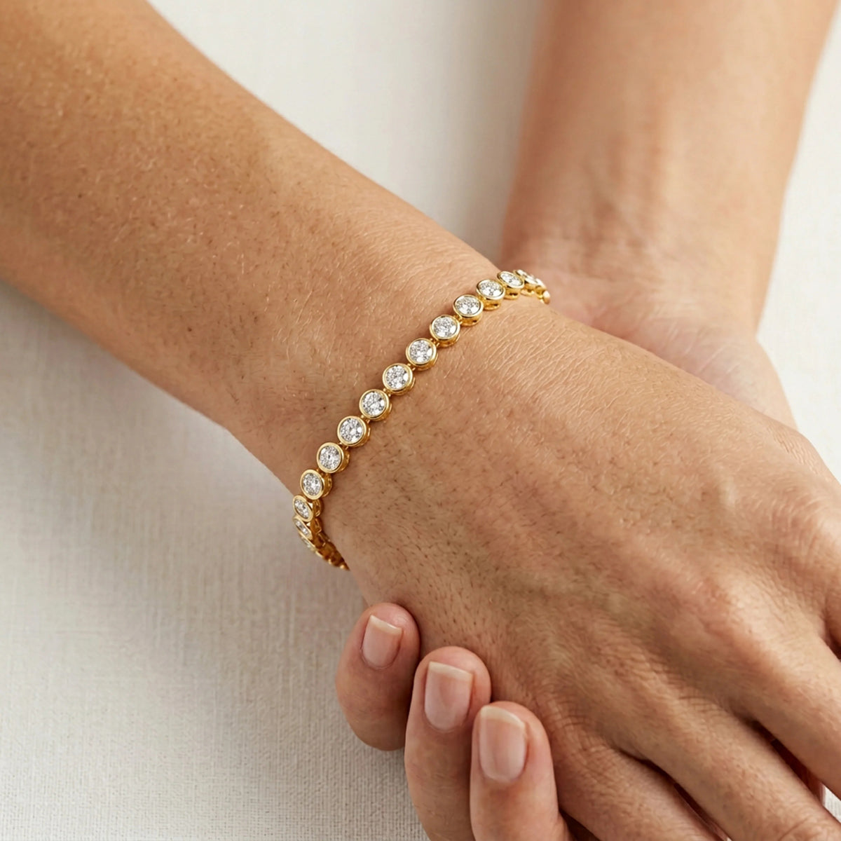 The ELLA STEIN - DIAMOND ESSENTIAL TENNIS BRACELET by ELLA STEIN features round, clear natural diamonds set in individual gold bezels, arranged in a single row with an adjustable chain and lobster clasp, displayed on a white background.