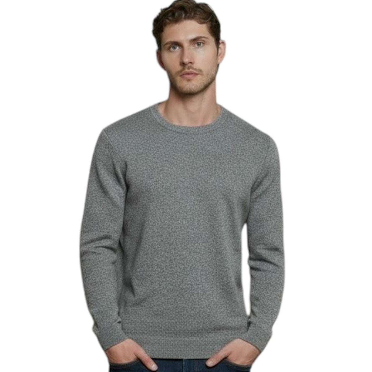 A man stands indoors in front of large windows, wearing the AUTUMN CASHMERE - CASHMERE BASIC CREW NECK WITH RIB BOTTOM IN STONE, paired with dark blue jeans and white sneakers. The cityscape visible outside the windows complements his refined taste in men’s knitwear from AUTUMN CASHMERE.