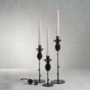 The ZODAX PINECONE WROUGHT IRON CANDLEHOLDER - MEDIUM features a black iron pine cone design atop a slender branch on a round base, measuring 4.5" x 13". Shown against a white background.