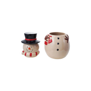 A CREATIVE COOP SNOWMAN JAR WITH LID, featuring a red scarf, black hat, and painted smile, is split in half on a beige surface with white pebbles spilling out between the head and body.