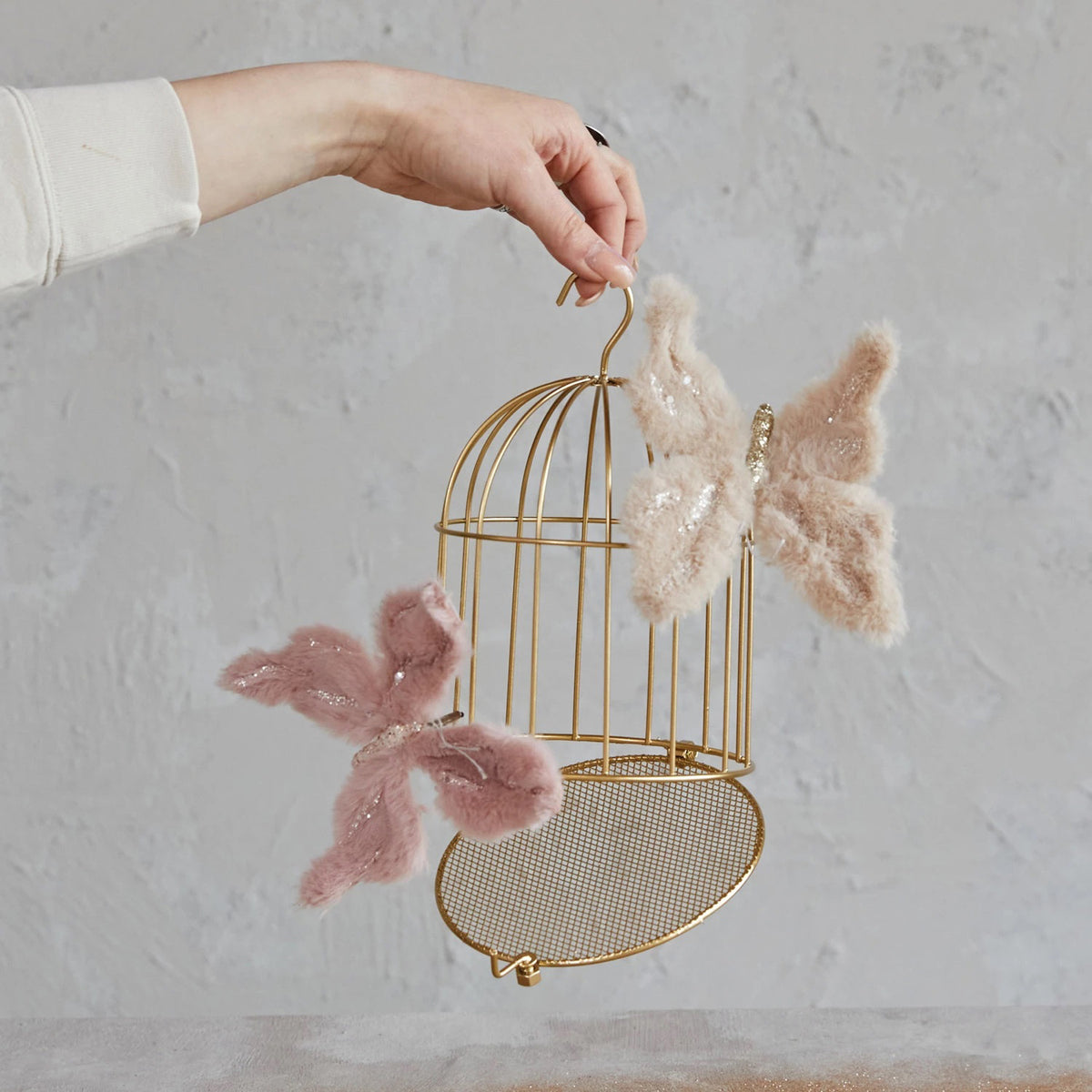 The METAL BIRD CAGE ORN by CREATIVE COOP features a golden finish with vertical bars and a domed top. Designed with a hook for hanging and a small latch-door at the bottom front, this elegant ornament stands gracefully on its base against a plain white backdrop.