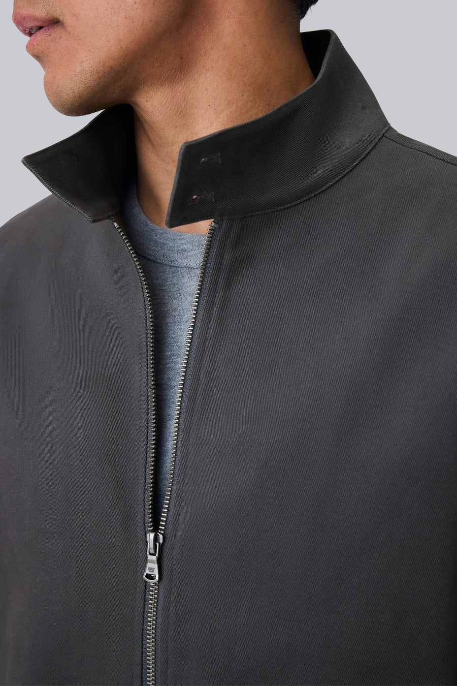 The MACK WELDON Twill Harrington Jacket in Asphalt is a dark gray cotton cavalry twill zip-up with a stand collar, two angled button-flap pockets, ribbed cuffs and hem, offering an English jacket style. Shown on a black background.