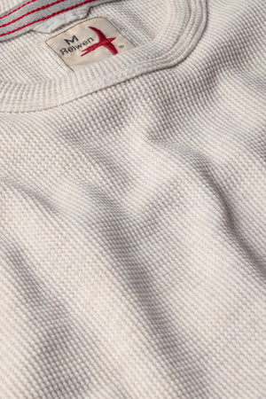 Close-up of the RELWEN Bi-Waffle Crew in Oatmeal, a textured off-white thermal shirt made from 100% cotton and featuring a visible collar along with a fabric tag labeled “RELWEN M” stitched with red thread.