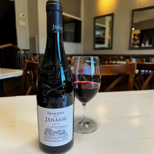 A bottle of JANASSE ‘TRADITION’ CHATEAUNEUF-DU-PAPE 2021 from WINE: FREEDOM BEVERAGE, featuring an embossed crest on the neck and a detailed illustration of a vineyard on the label.