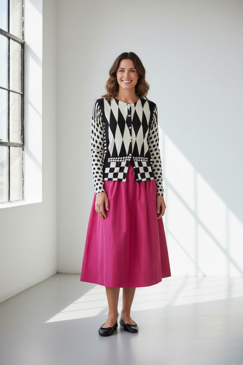 Wearing the IN BED WITH YOU - GEOMETRIC PRINT CARDIGAN by IN BED WITH YOU/CLAUDIOLAI SRL in cotton silk with diamond, checkered, and polka dot designs, paired with a bright pink skirt against a plain white background.