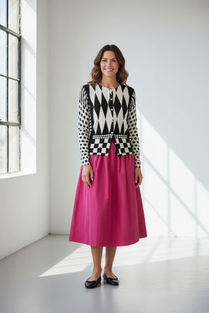 Wearing the IN BED WITH YOU - GEOMETRIC PRINT CARDIGAN by IN BED WITH YOU/CLAUDIOLAI SRL in cotton silk with diamond, checkered, and polka dot designs, paired with a bright pink skirt against a plain white background.