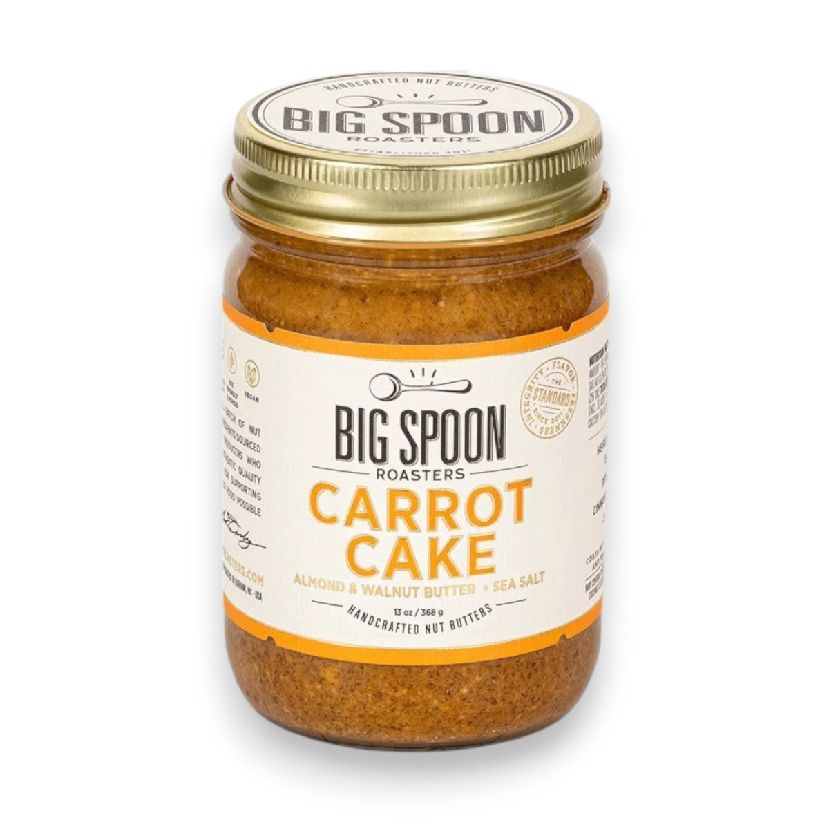 A 13-ounce (369 grams) jar of BIG SPOON ROASTERS - CARROT CAKE nut butter with sea salt. The jar features a white label adorned with orange accents and the BIG SPOON ROASTERS logo at the top. This vegan, handcrafted spread, rich in heart-healthy fats, is sealed with a gold lid.