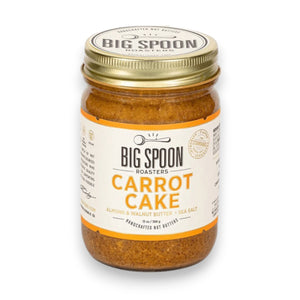 A 13-ounce (369 grams) jar of BIG SPOON ROASTERS - CARROT CAKE nut butter with sea salt. The jar features a white label adorned with orange accents and the BIG SPOON ROASTERS logo at the top. This vegan, handcrafted spread, rich in heart-healthy fats, is sealed with a gold lid.