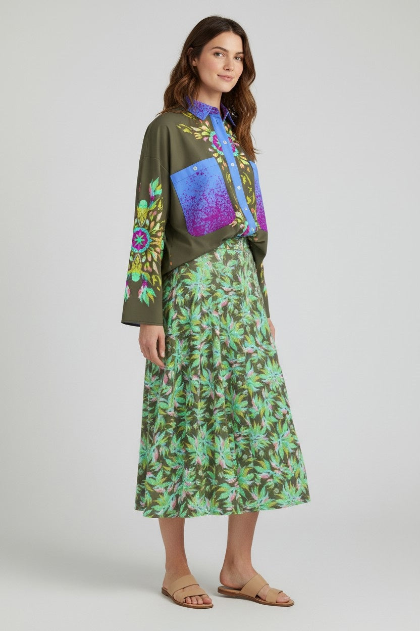A woman with long brown hair, smiling slightly, wears a loose-fitting, long-sleeve top with colorful patterns, the FRANCO FERRARI Floral Print Skirt from Italy in green, and beige sandals.