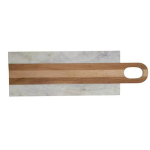 A kitchen scene features four BE HOME - MOA MARBLE & WOOD LONG BOARDS by BE HOME, INC, surrounded by herbs, sliced lemon, cherry tomatoes, olive oil, spice jars, a glass of wine, and bread on a beige countertop against a textured beige wall.