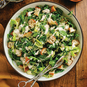 Person standing on a porch in front of a light blue house with a white door.