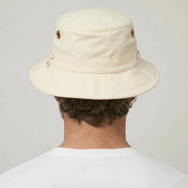 A bearded man in a white shirt wears the TILLEY - ICONIC T1 BUCKET HAT IN NATURAL with UPF 50+ protection and metal eyelets, looking directly at the camera against a plain background.